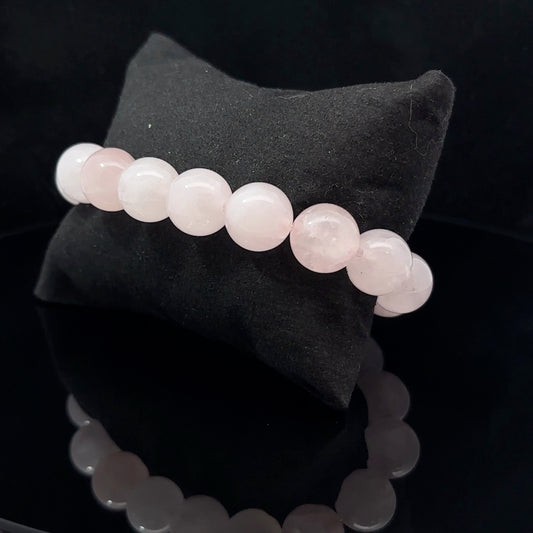 A bracelet made of pink quartz displayed on a black background, with a black pillow behind it.