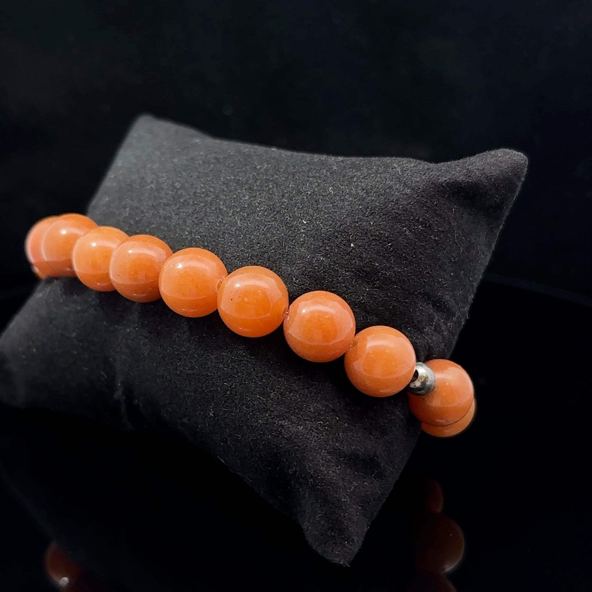 An orange aventurine bead bracelet placed on a black textured surface.