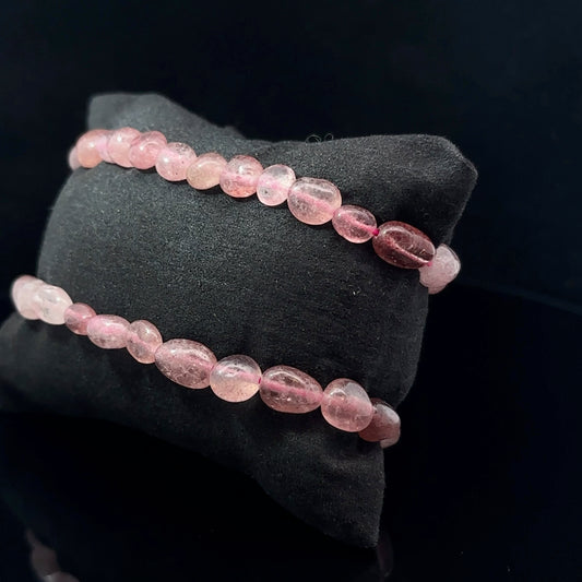 A bracelet composed of pink and red tumbled quartz crystals with a black fabric background.