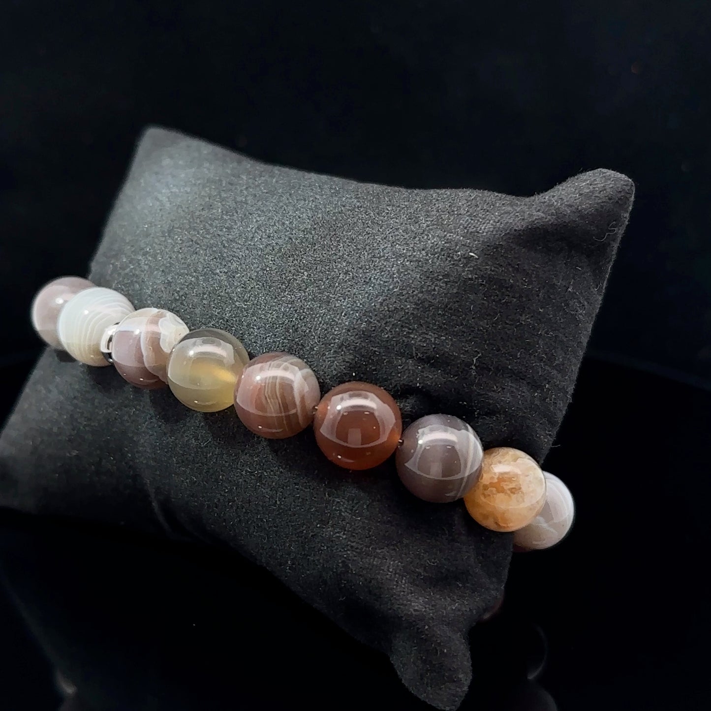 A multicolored agate bead bracelet with varying shades of gray, beige, and brown, displayed on a dark background.