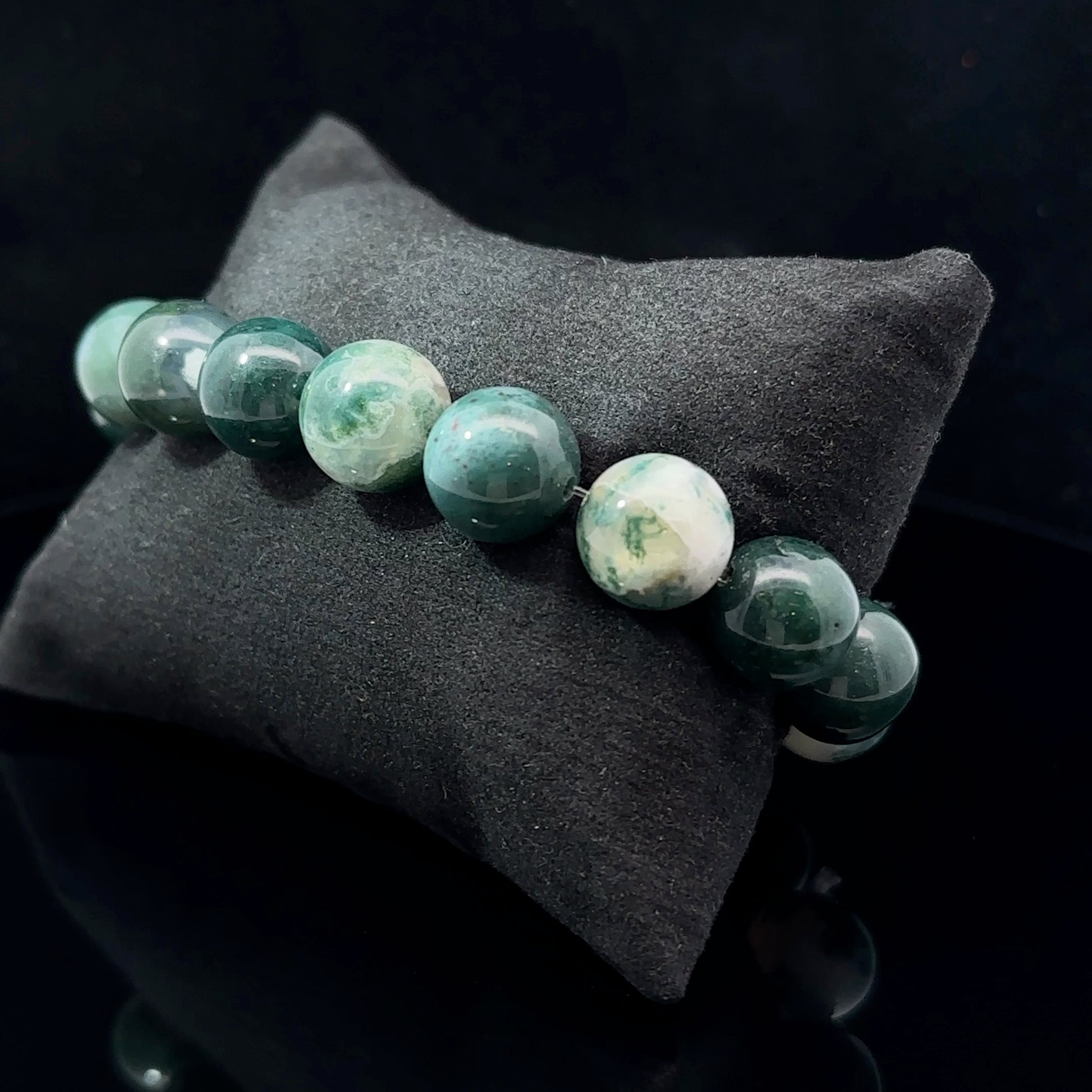 A bracelet with a series of oval-shaped beads featuring a mocha color, placed on a dark textured surface.