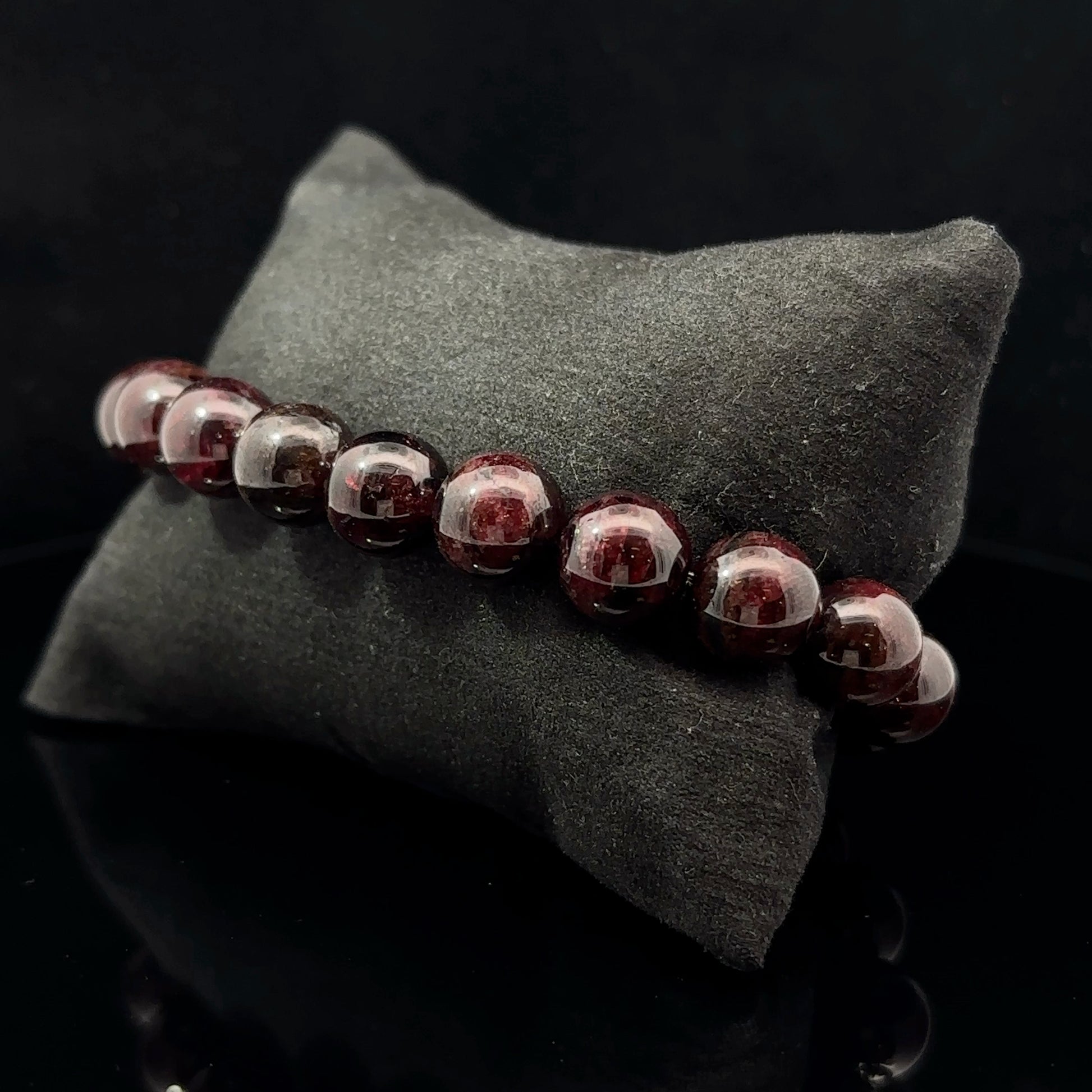 A bracelet with a series of round red beads on a dark background, placed on a black textured surface.