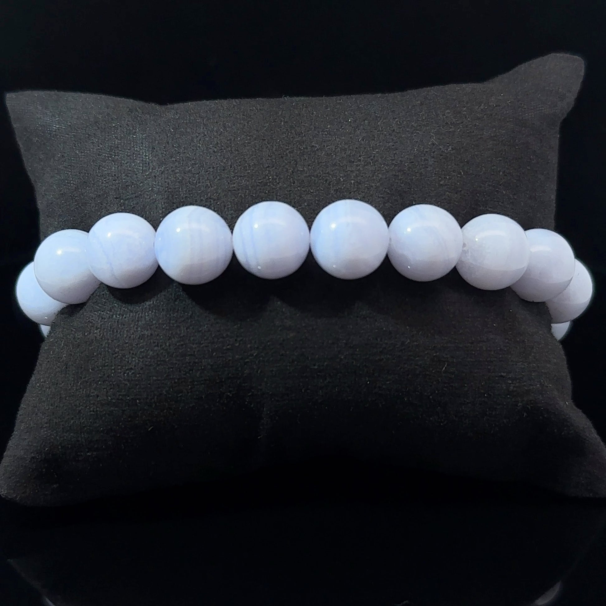 A bracelet with white and blue agate beads, displayed on a dark background