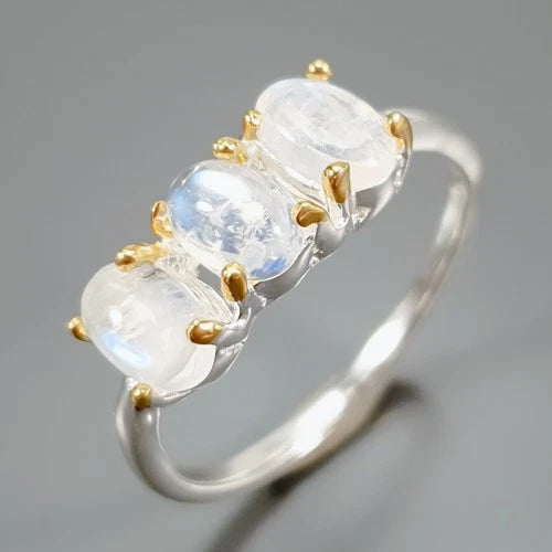 Ring with three moonstone stones and gold prongs on a gray background