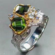 Load image into Gallery viewer, Elegant ring with green gemstone, gold accents, and clear stone on a gray background
